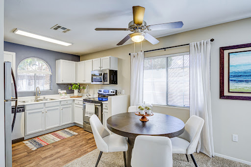 A bright and modern kitchen with a cozy dining area, featuring white cabinetry and a ceiling fan.