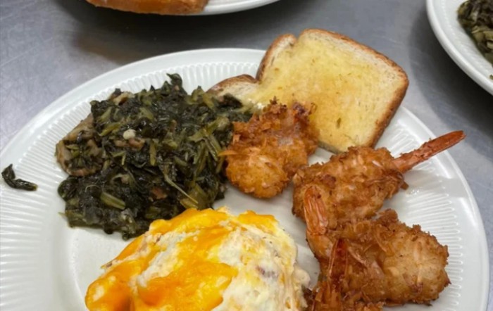 A plate of comfort food including fried chicken, cheesy dish, greens, and bread.