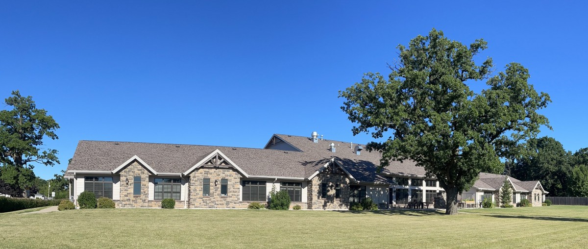 A stone facade house with a large lawn and a tree under a clear blue sky.