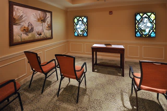 A small, warmly lit room with four chairs facing a table and decorative stained glass windows.