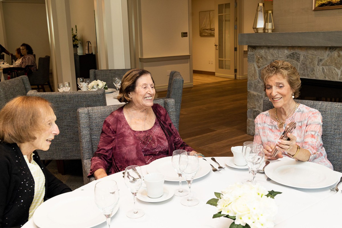A group of women enjoying a dinner gathering, smiling and sharing conversation.
