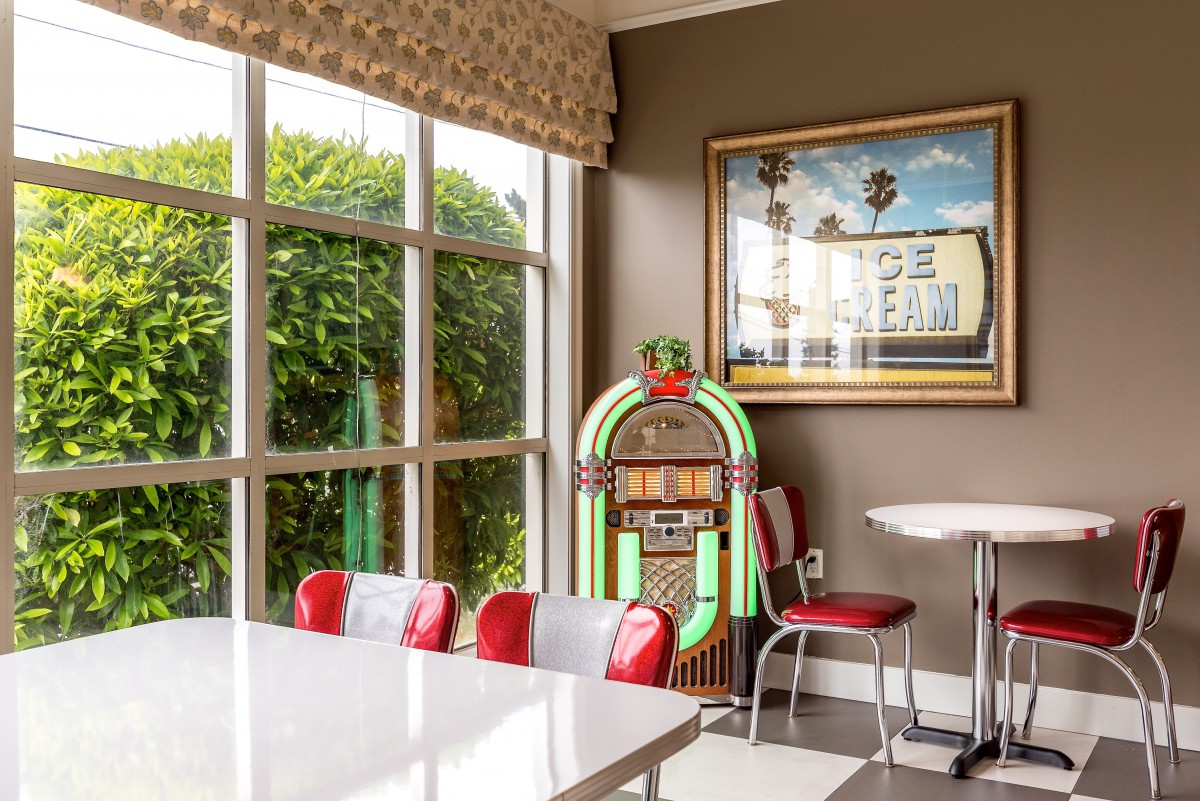 A retro diner interior featuring a classic jukebox and red seating by a large window.