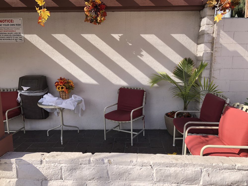 A cozy outdoor patio with chairs, a small table, and decorative plants under the shade.