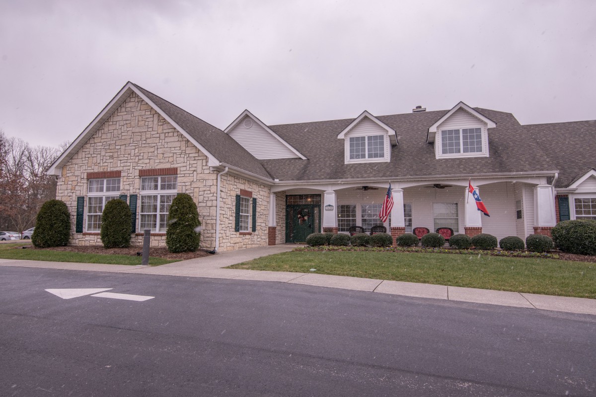 A residential building with a stone facade and a well-maintained front yard under a cloudy sky.