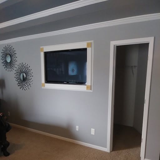 A living room with a wall-mounted TV and decorative art on gray walls.