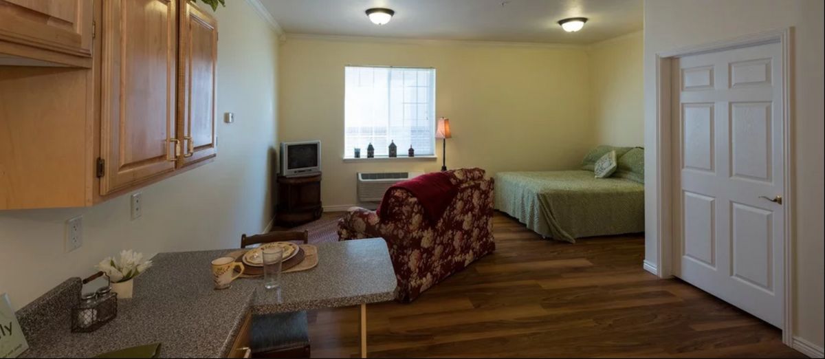 A cozy studio apartment with a bed, armchair, and television.