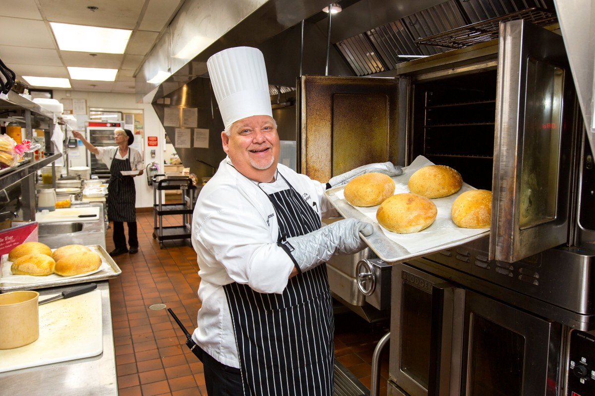 A chef proudly displays freshly baked bread in a professional kitchen.