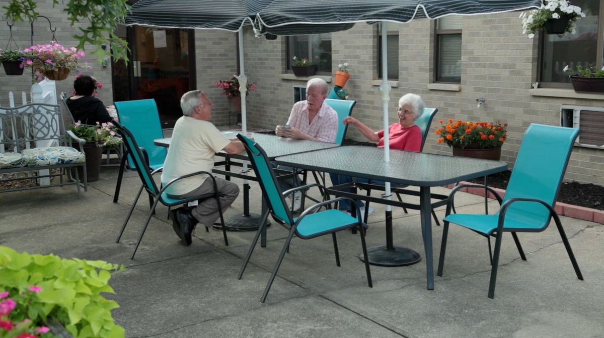 A group of people sitting and conversing at an outdoor patio table under a canopy.