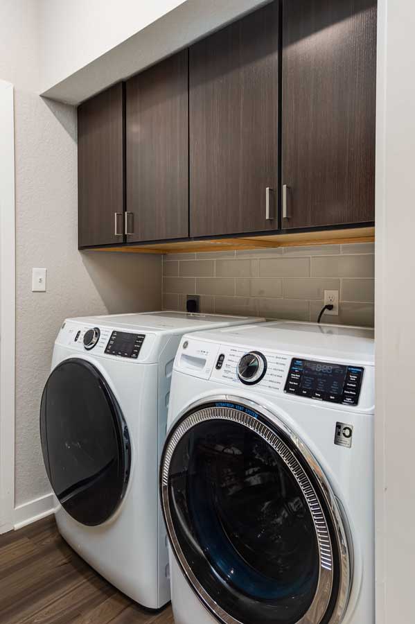 A modern laundry room with a washing machine and dryer beneath dark wooden cabinets.