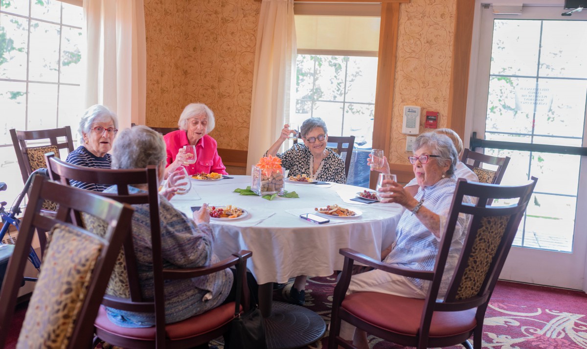 A group of elderly women enjoying a meal and conversation around a dining table.