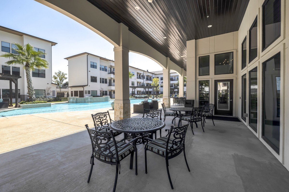 Outdoor patio area with seating overlooking a pool at an apartment complex.