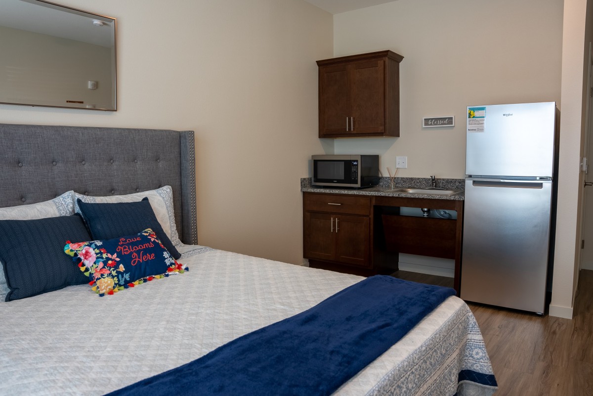 A cozy hotel room with a bed, microwave, and refrigerator.