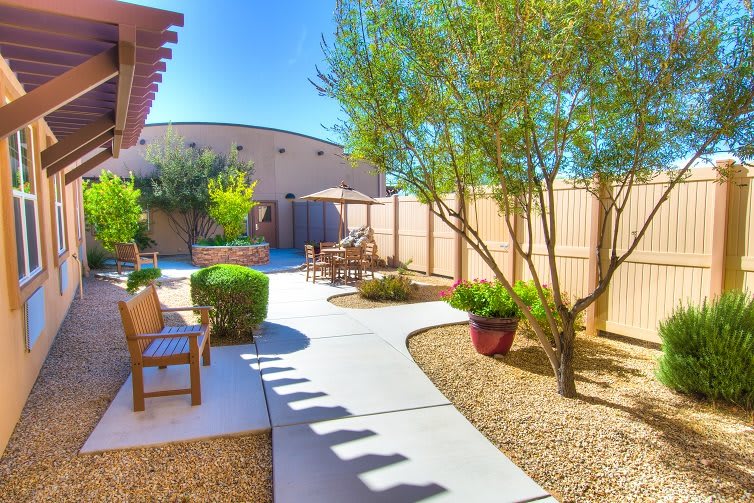 A beautifully landscaped backyard with a paved pathway, desert-friendly plants, and patio furniture on a sunny day.