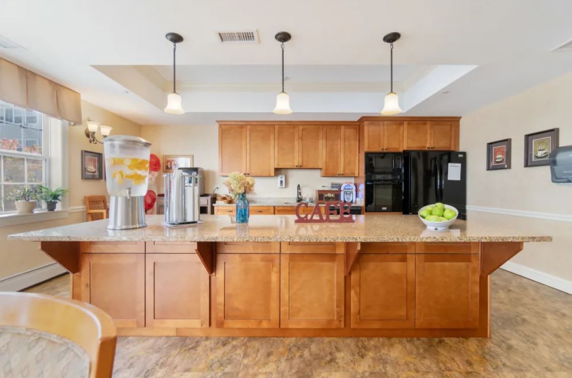 A modern kitchen with wood cabinets, featuring a coffee station and pendant lighting.