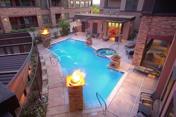 An inviting outdoor pool area with a fire feature and surrounding buildings, illuminated at night.