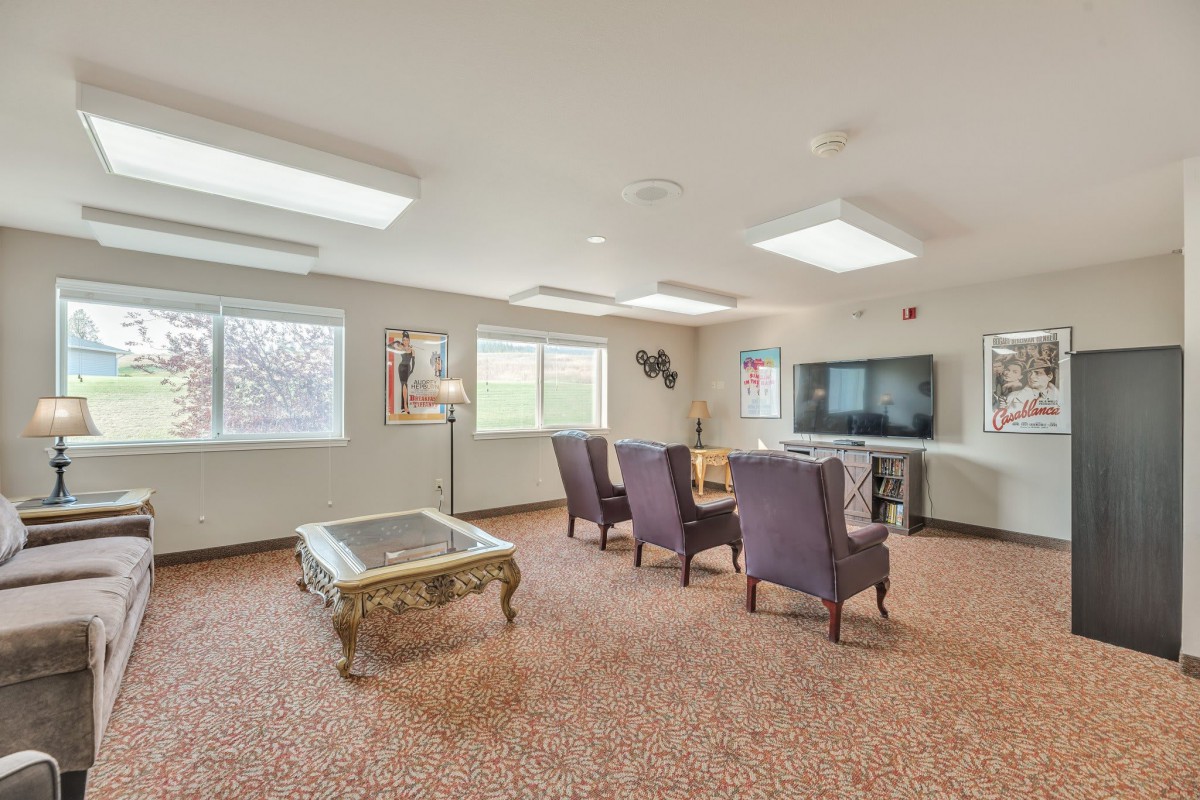A spacious living room with several upholstered chairs, a coffee table, and a large television.