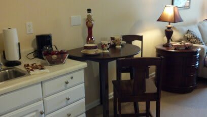 A cozy dining area with a small table and two chairs, adorned with a lamp and decorative items.