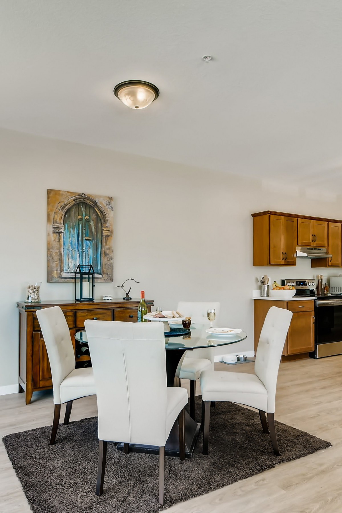 A modern dining space with a round glass table and upholstered chairs, adjacent to a kitchen area with wooden cabinets.