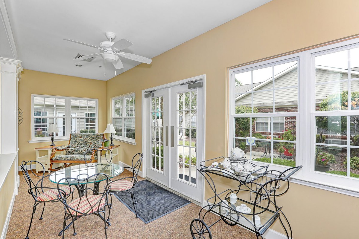 A cozy sunroom filled with natural light, featuring a table with chairs and large windows.