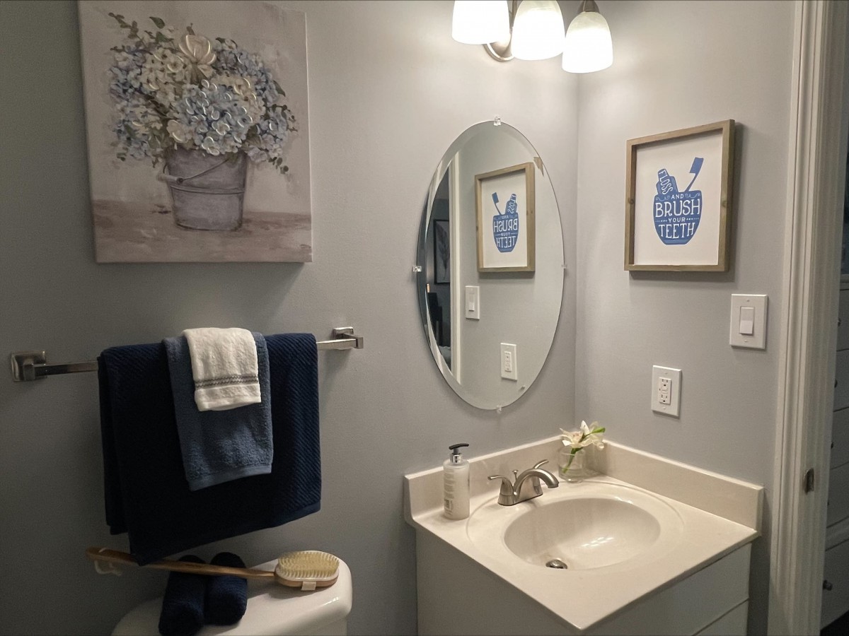 A neatly organized bathroom with a mirror, sink, and decorative wall art.