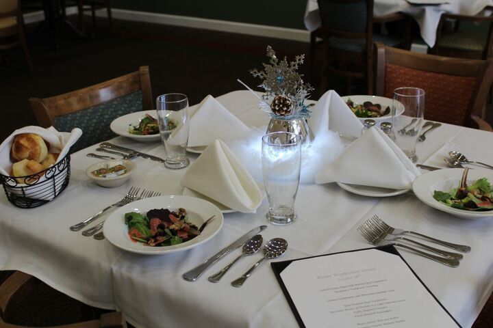 A formal dining table set with plates of food, glassware, and a decorative centerpiece.