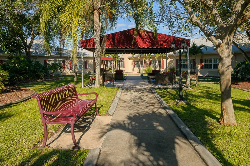 A peaceful park setting with a pathway, bench, and gazebo surrounded by palm trees.