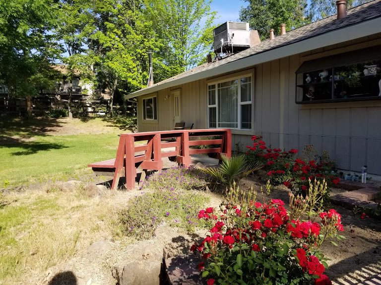 A peaceful backyard view featuring a house with a wooden deck and vibrant red flowers.