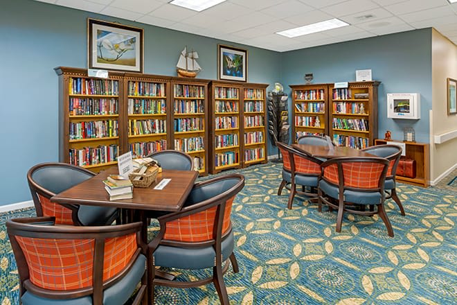 A cozy library reading area with bookshelves, tables, and chairs.