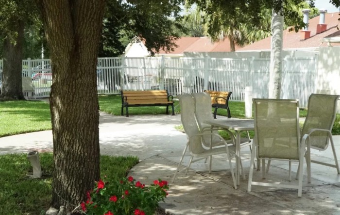 A serene garden setting with outdoor chairs and benches surrounded by trees and flowers.
