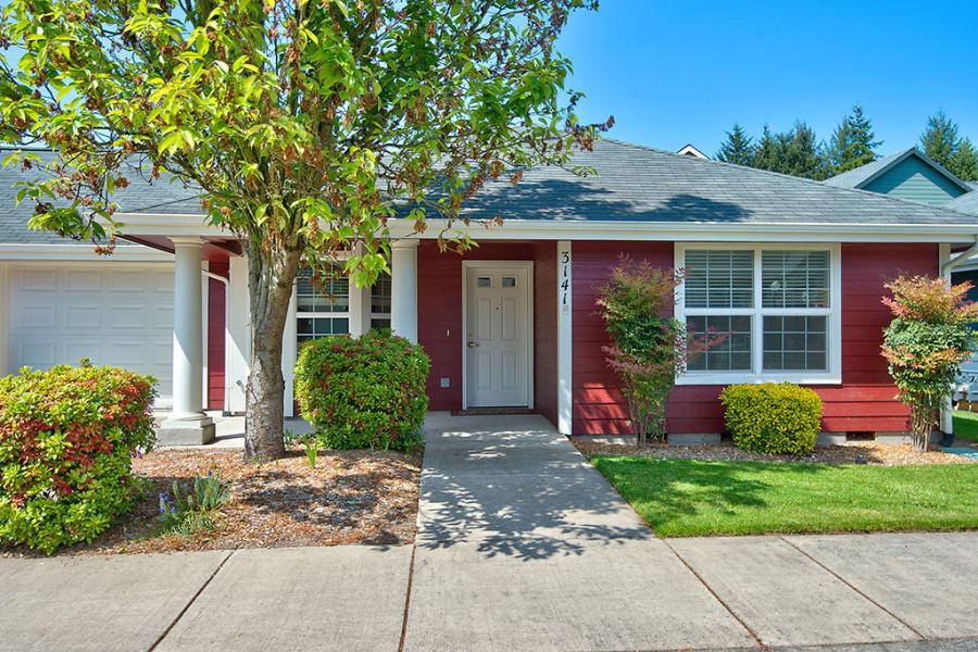 A charming single-story red house with a tidy front yard and a clear sidewalk.