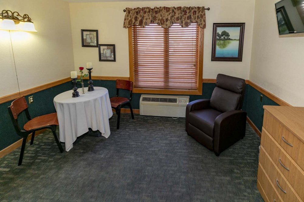 A cozy living room setup with a table and chairs, an armchair, and framed pictures on the walls.