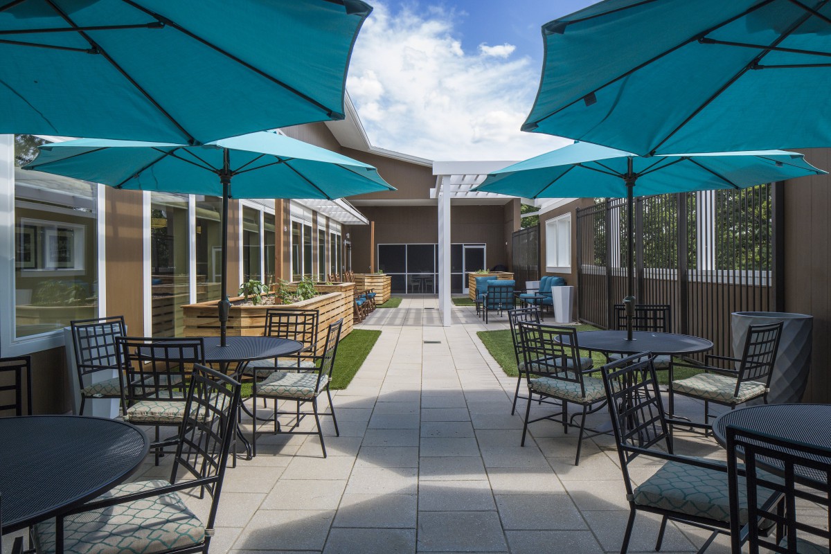 A modern outdoor patio area with blue umbrellas and neatly arranged tables and chairs under a clear sky.