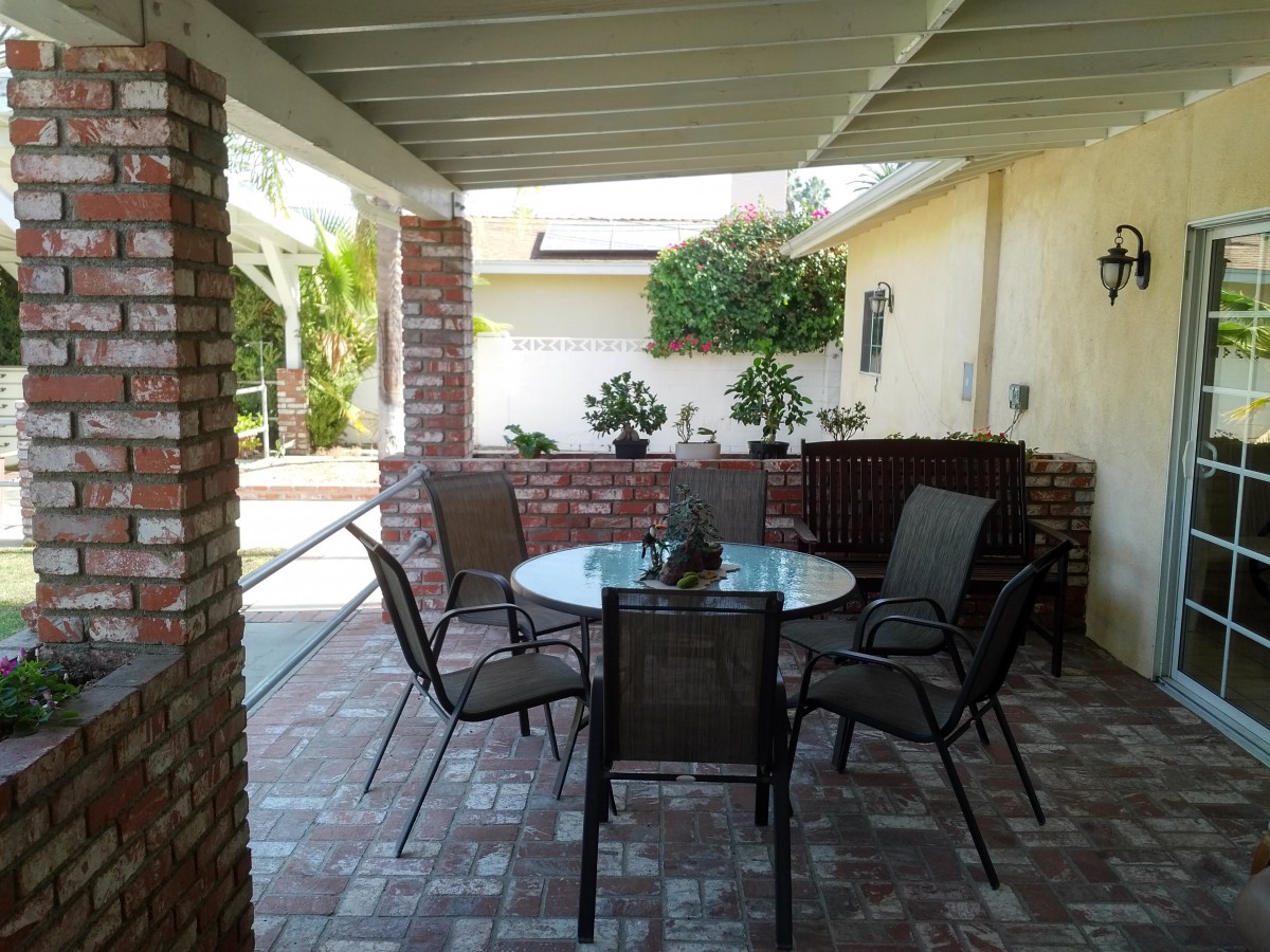 A cozy patio with a glass table surrounded by chairs, framed by brick walls and greenery.