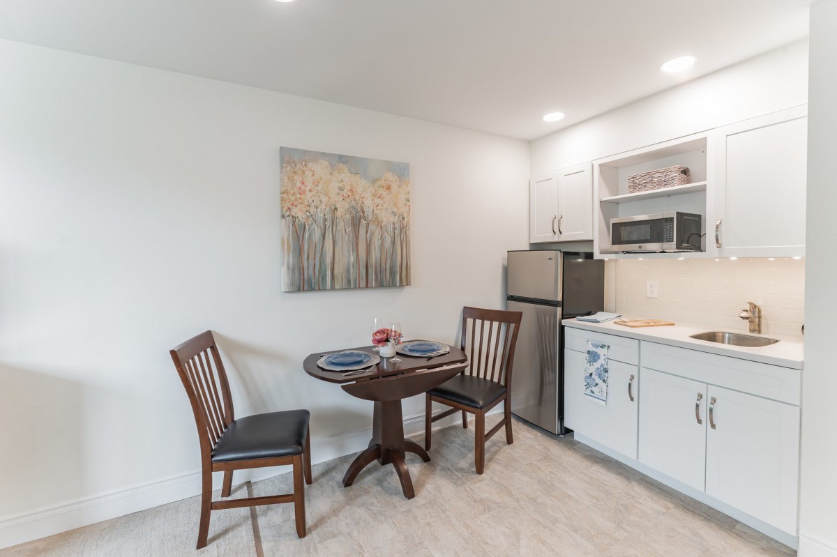 A cozy kitchen and dining area featuring a small round table with two chairs, modern appliances, and minimalist wall art.