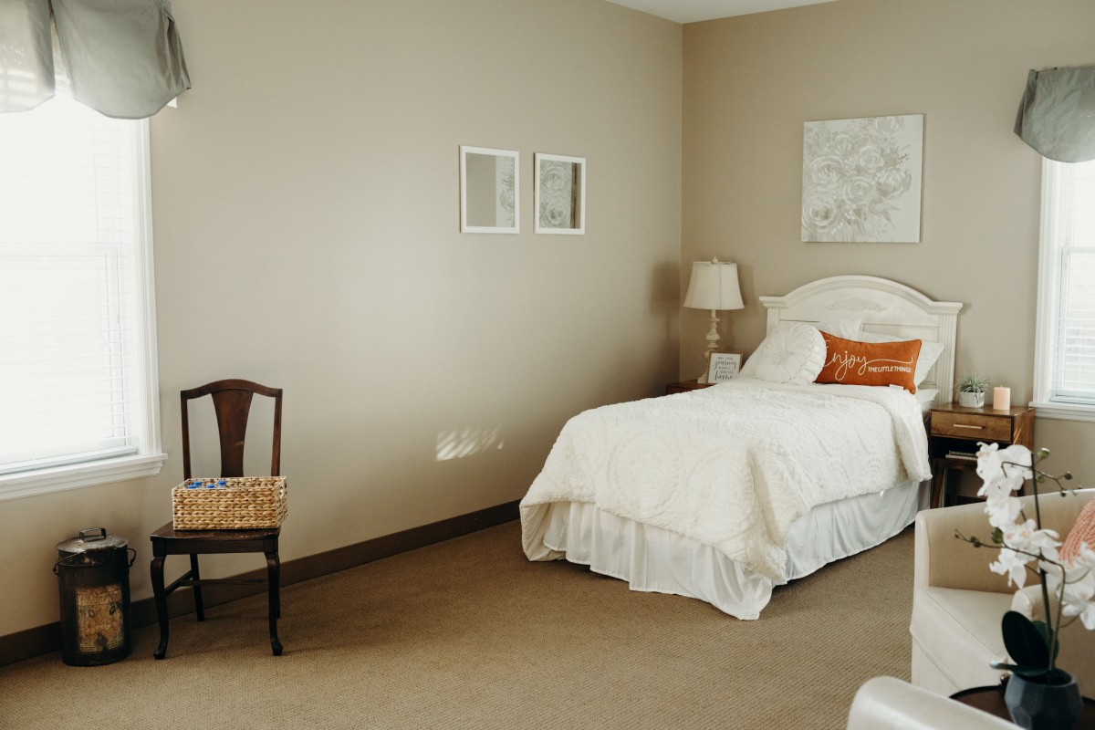 A minimalist bedroom with a single bed, lamp, and chair.