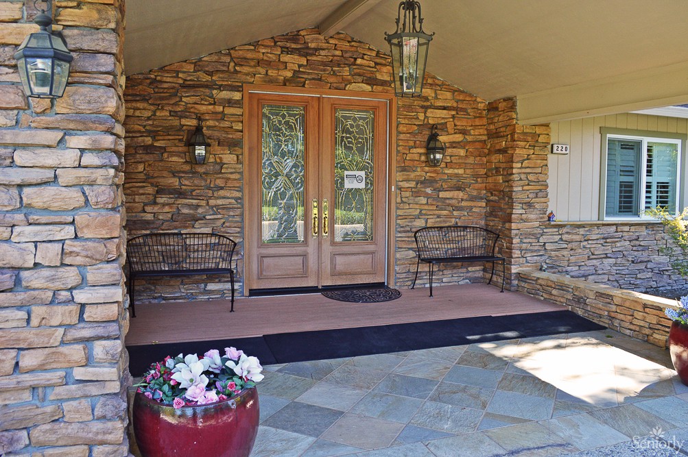 A welcoming front porch featuring stone walls, double wooden doors, and a potted plant.