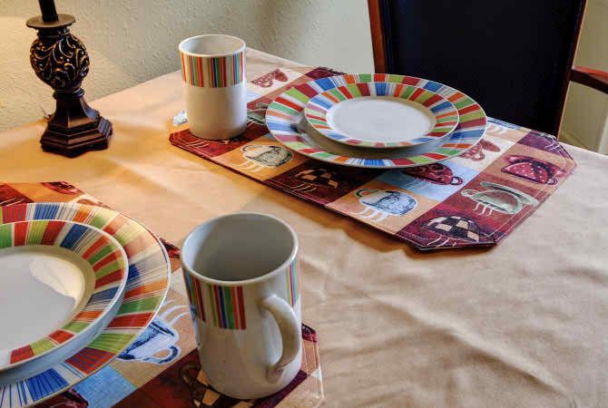 A dining table set with striped mugs and plates on colorful placemats.