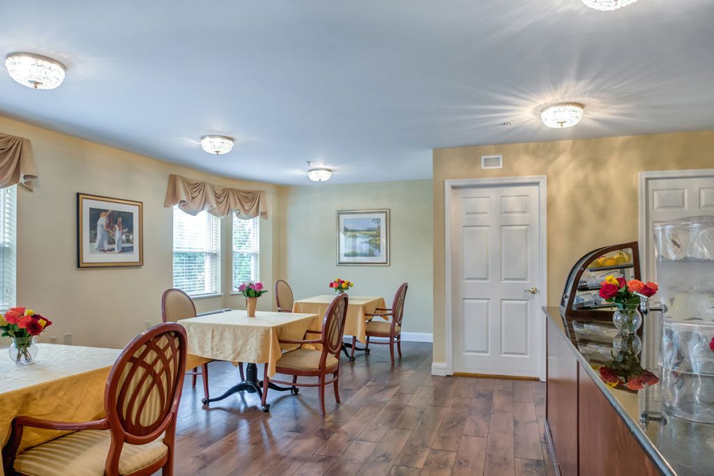 A cozy dining room with tables and chairs, featuring hardwood floors and soft lighting.