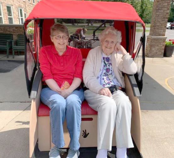 Two elderly women sitting together under a red canopy outdoors.