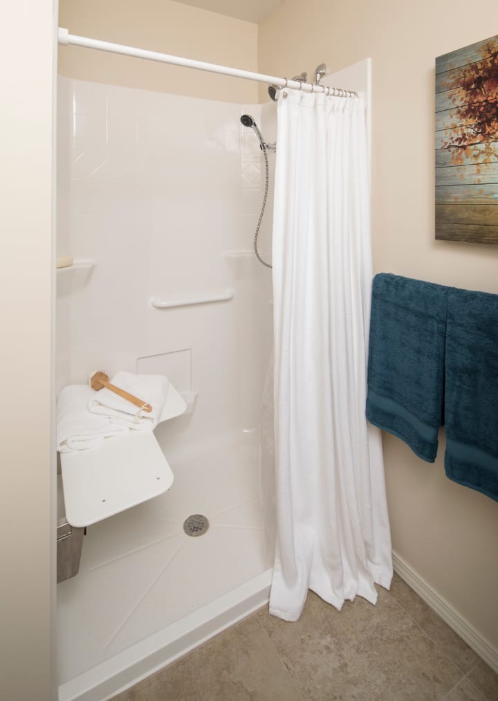 A bathroom shower with a white curtain, teal towels, and an accessible seat.