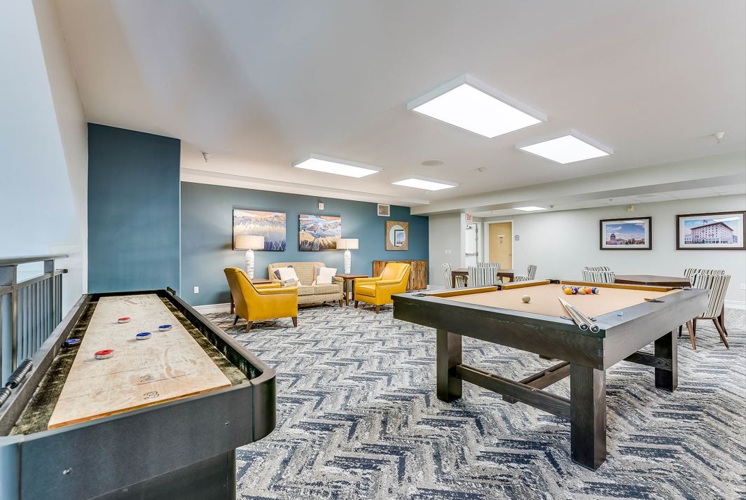 A modern game room featuring a pool table, shuffleboard, and comfortable seating.