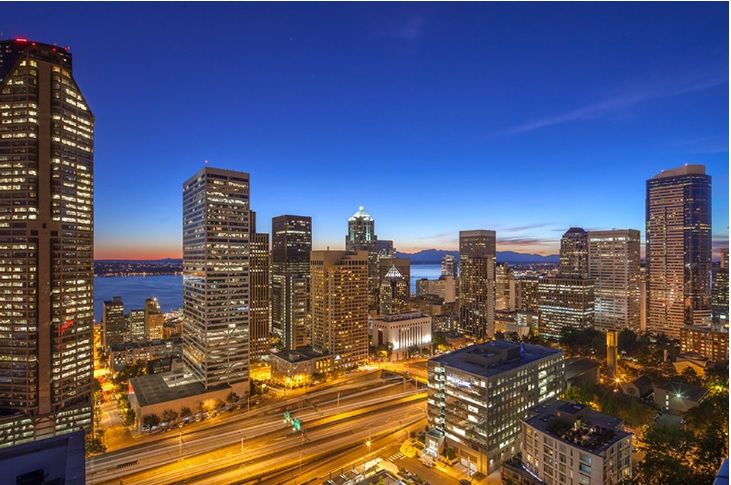 A stunning view of a city skyline illuminated at night, showcasing tall buildings and vibrant lights against a clear sky.