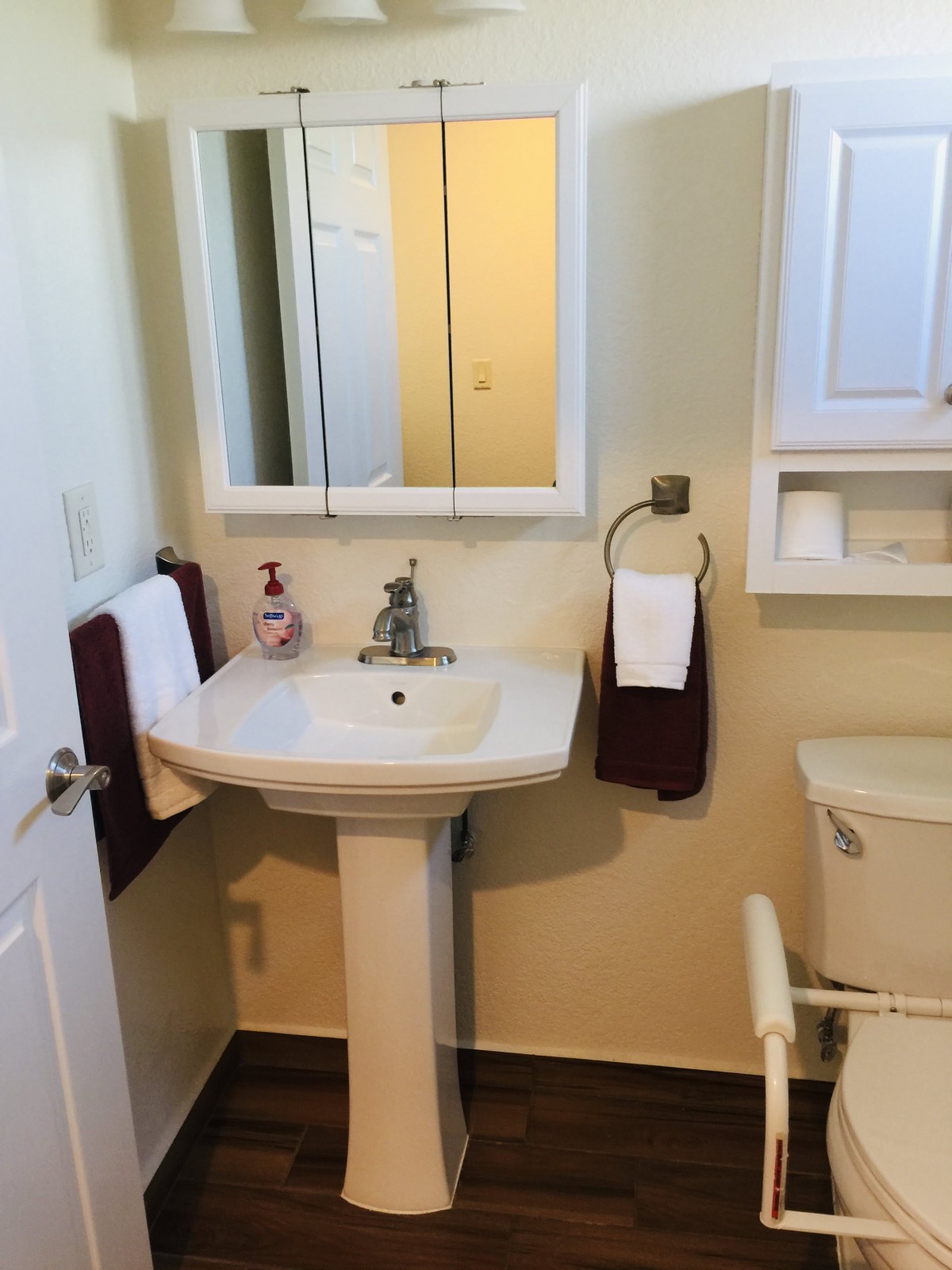 A clean and organized bathroom with a pedestal sink, mirror, and neatly hung towels.