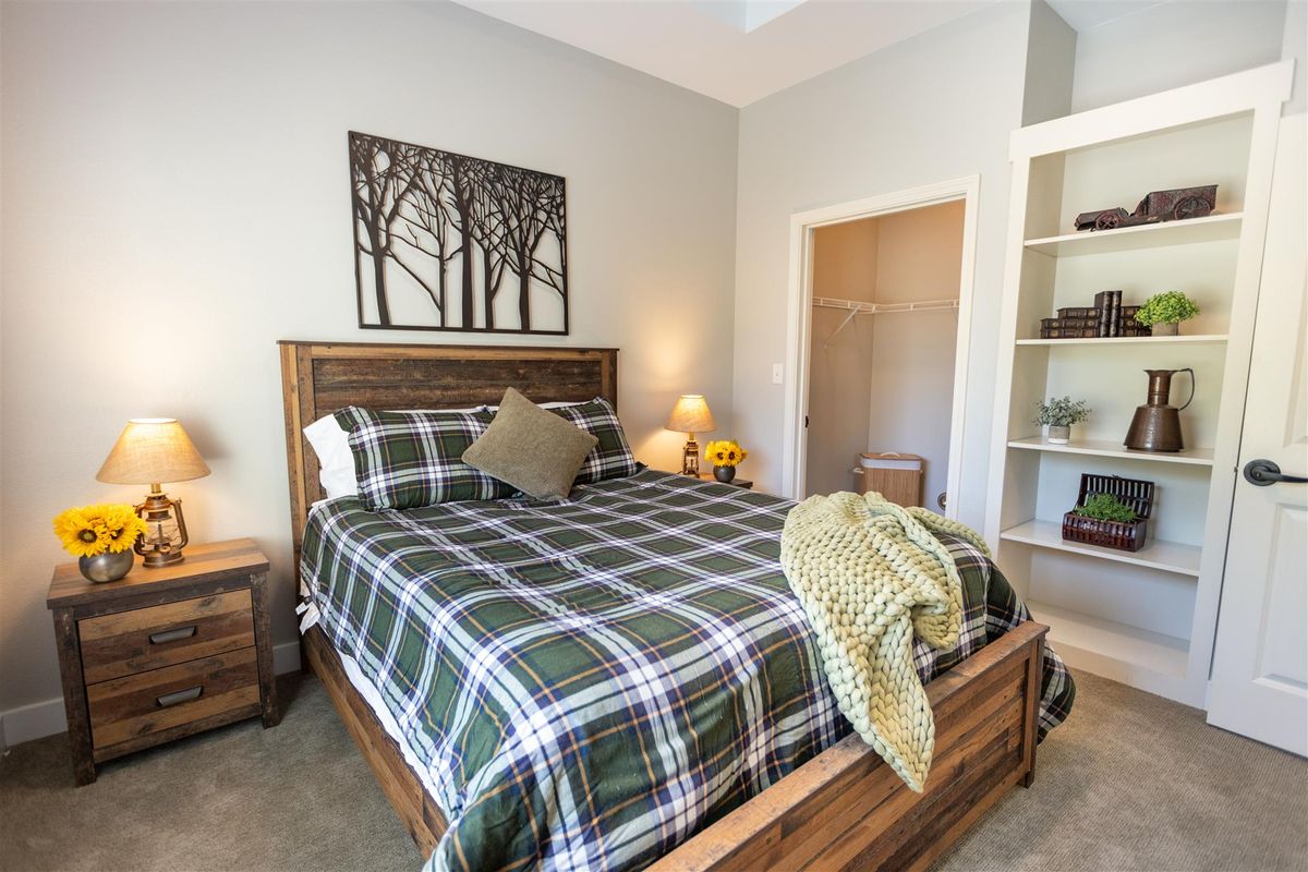 A cozy bedroom with a wooden bed frame and plaid bedding, featuring warm lighting and nature-themed wall art.