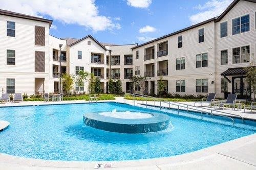 A modern apartment complex with a central swimming pool and clear skies.