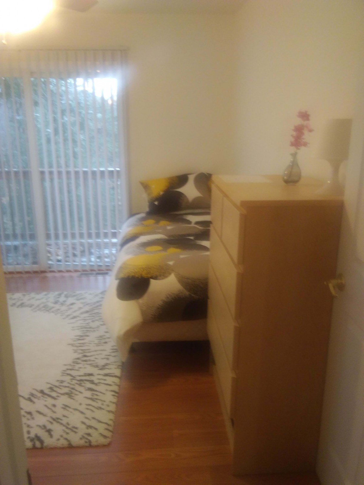A cozy bedroom featuring a bed with patterned bedding, a tall dresser, and a small lamp.