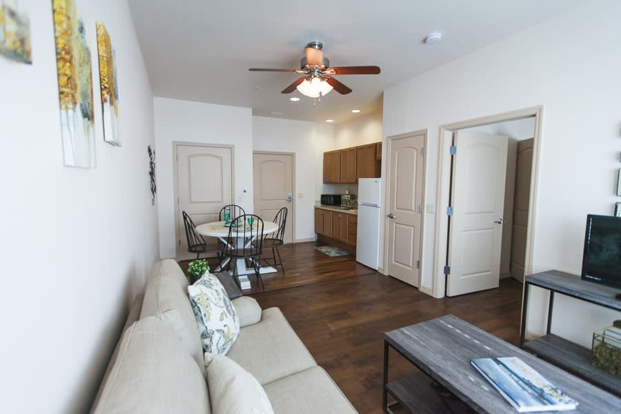 A cozy living area with a connected kitchen and dining space featuring a beige sofa, wooden furniture, and ceiling fan.