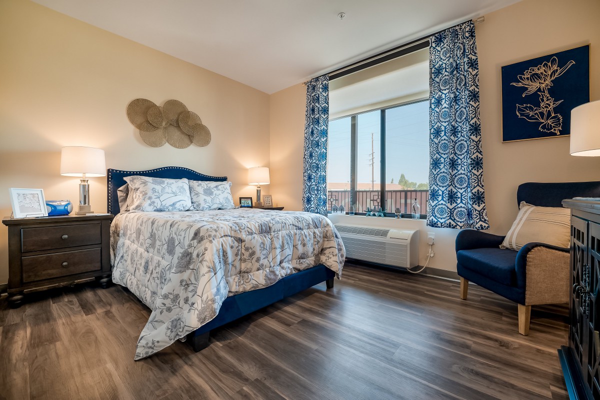A stylishly decorated bedroom with a cozy bed, large window, and modern furnishings.