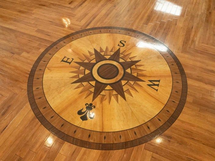A decorative compass rose inlaid on a wooden floor, showing the cardinal directions.