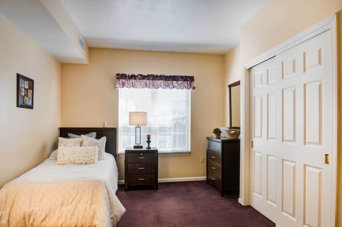 A cozy bedroom with a neatly made bed, nightstands, and a dresser under a window.